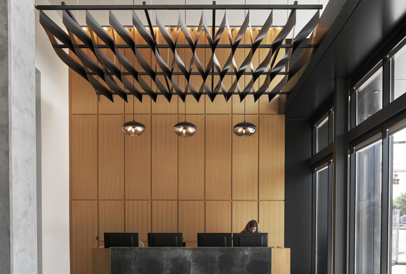 This front desk area features four computers, large windows, three hanging light fixtures and black Arktura panels above the desk. A person is standing behind the desk working.