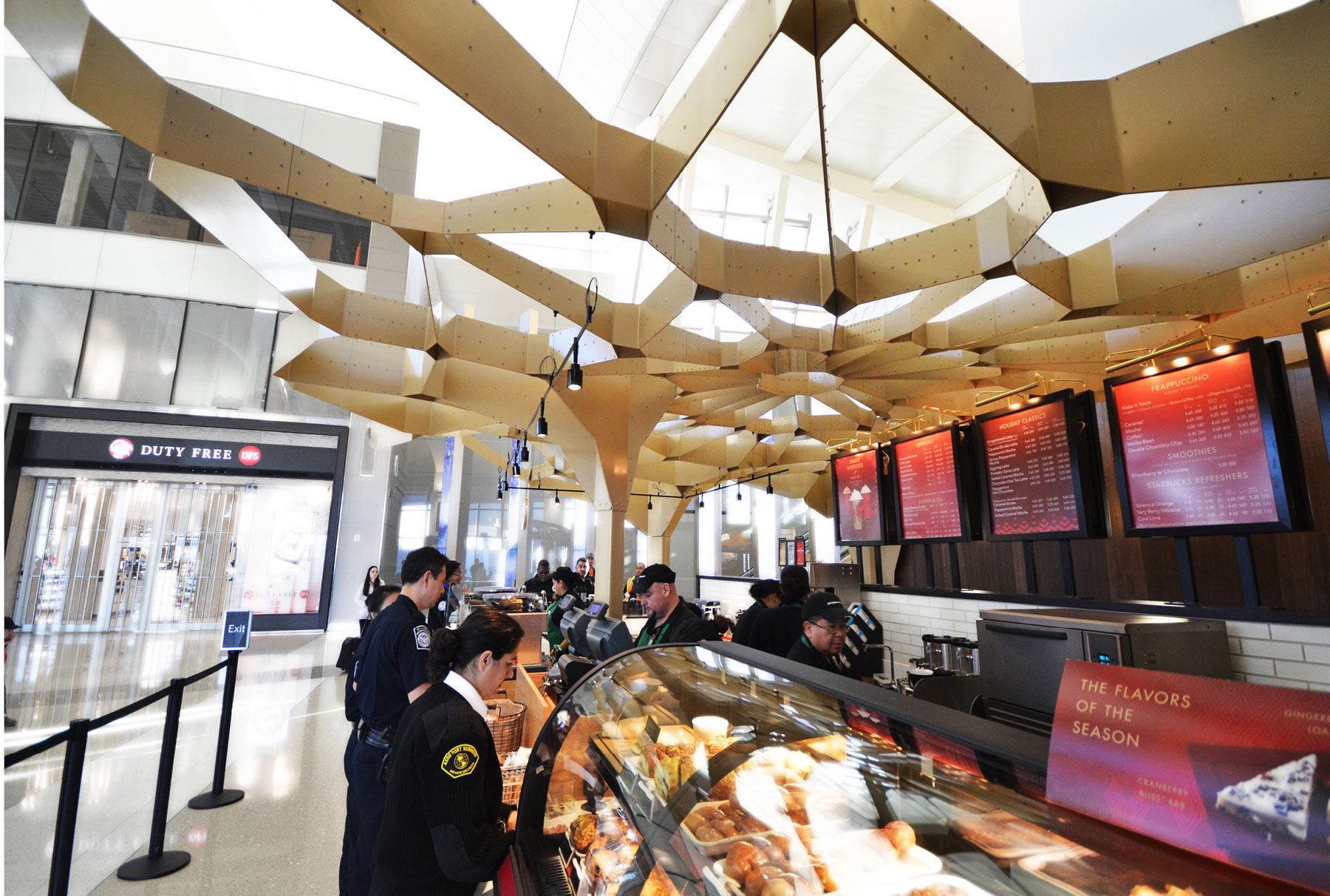 This Starbucks in LAX Airport features an Arktura ceiling canopy. There are people standing in line ordering. 