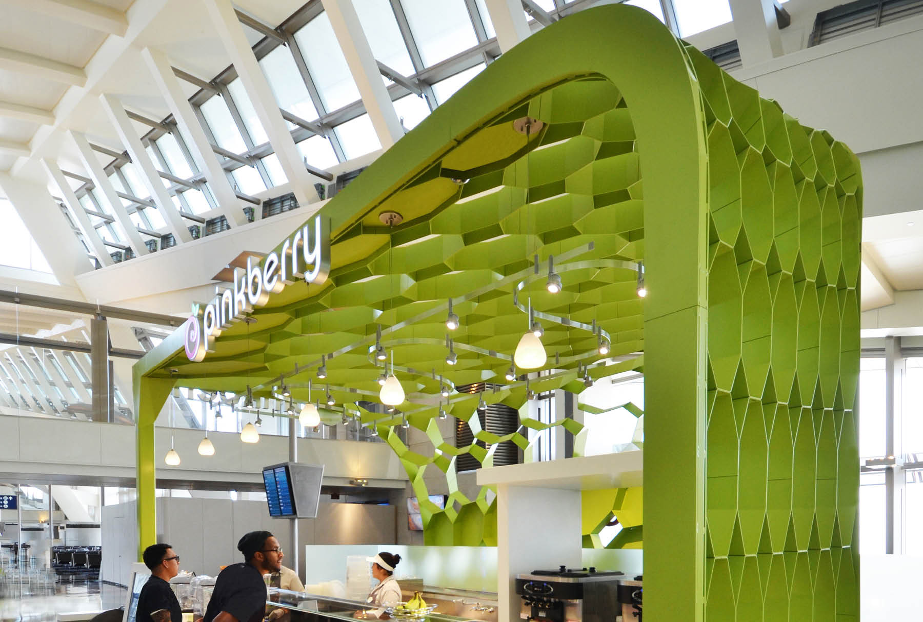 This Pinkberry location in the LAX Airport features a green Arktura canopy. There are people in line to order. 