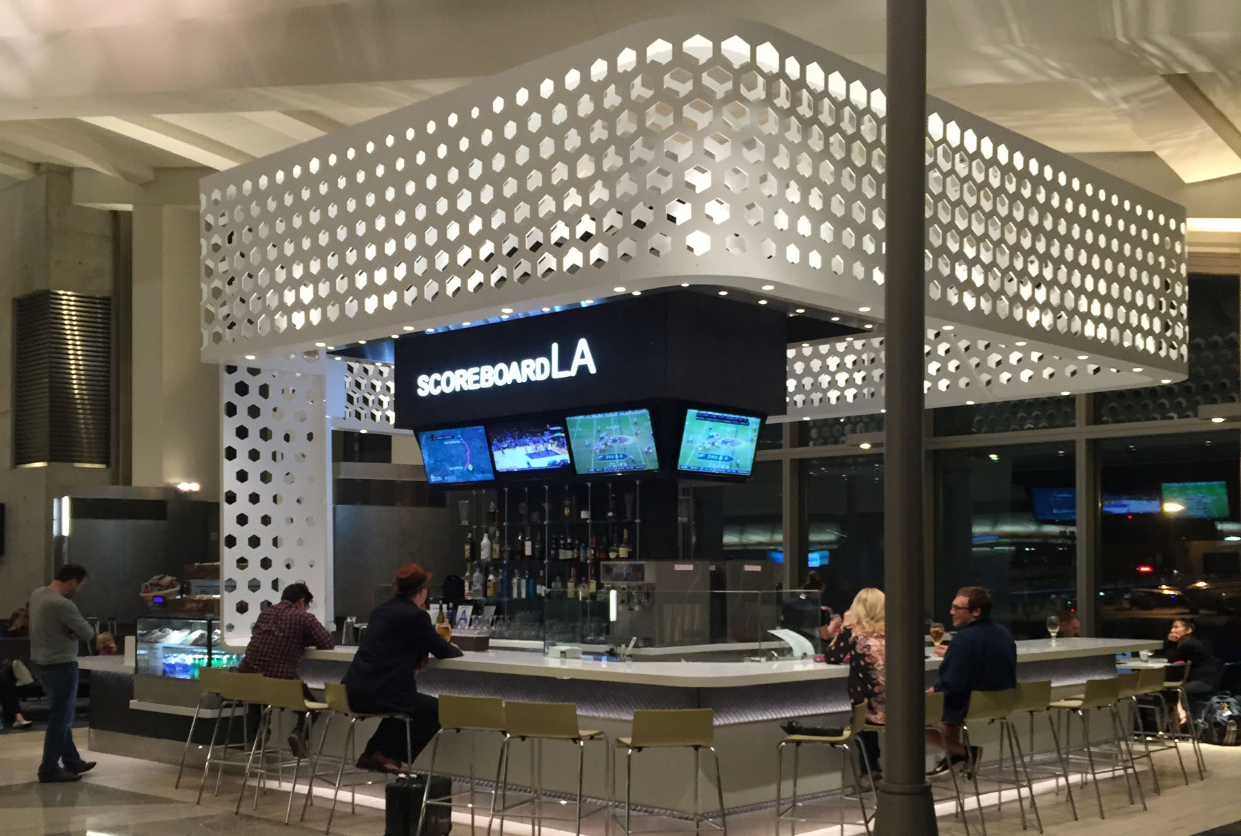  This Scoreboard sports bar in LAX Airport features an Arktura canopy above the bar area. There are four people sitting at the bar. 