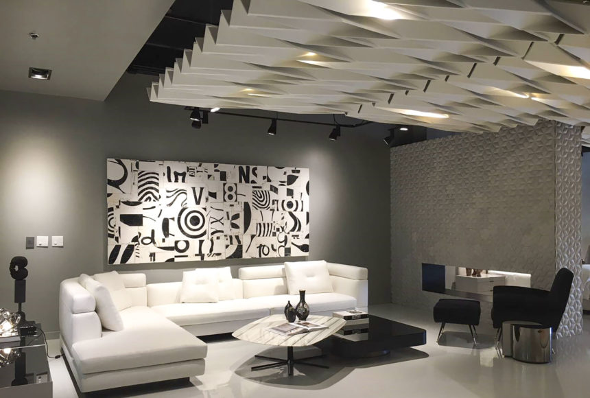 This room has white acoustic ceiling panels. There is a white couch and pillows as well as black and white artwork and a black chair.