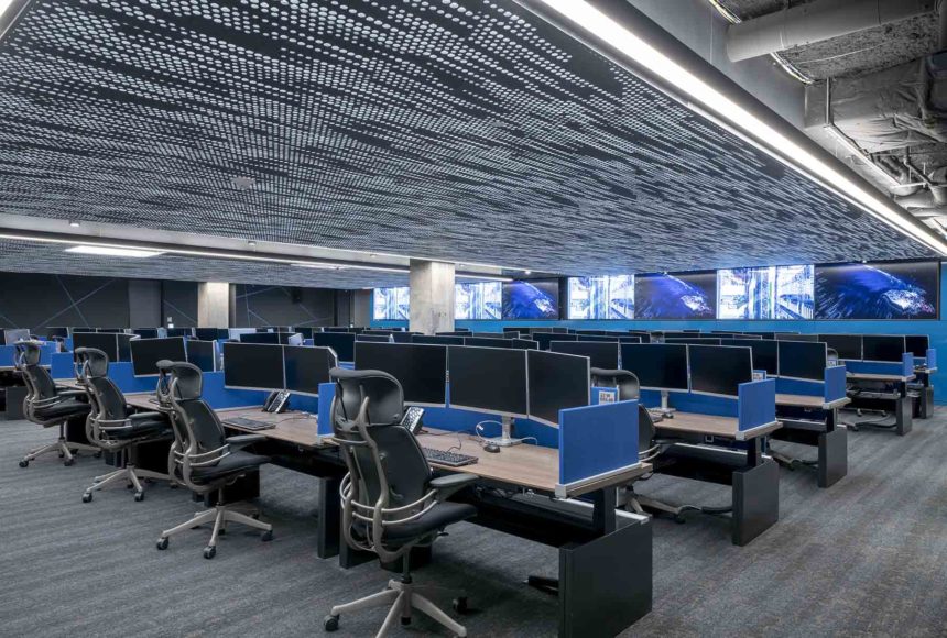 This office space embraces technology, with each seating station having three computer monitors. There are black and silver rolling chairs at each station. 
