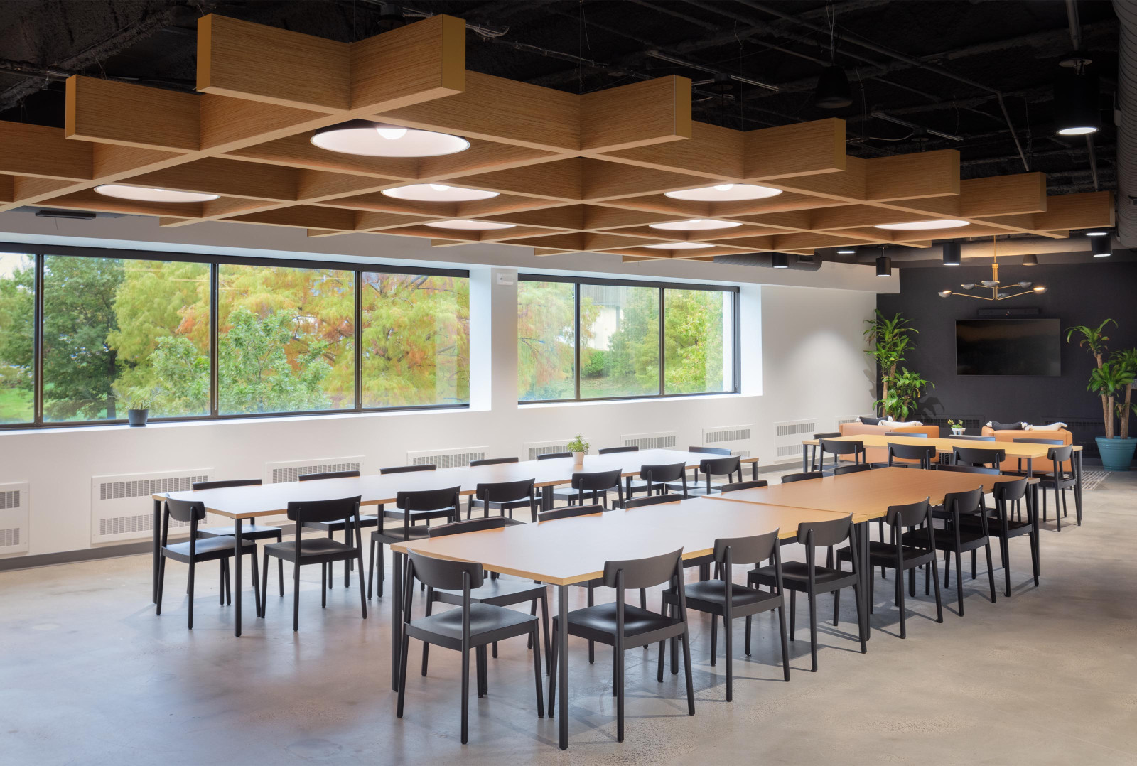 A conference room has two long tables with various black chairs. The ceiling’s panel system mimics the look of a wooden trellis.