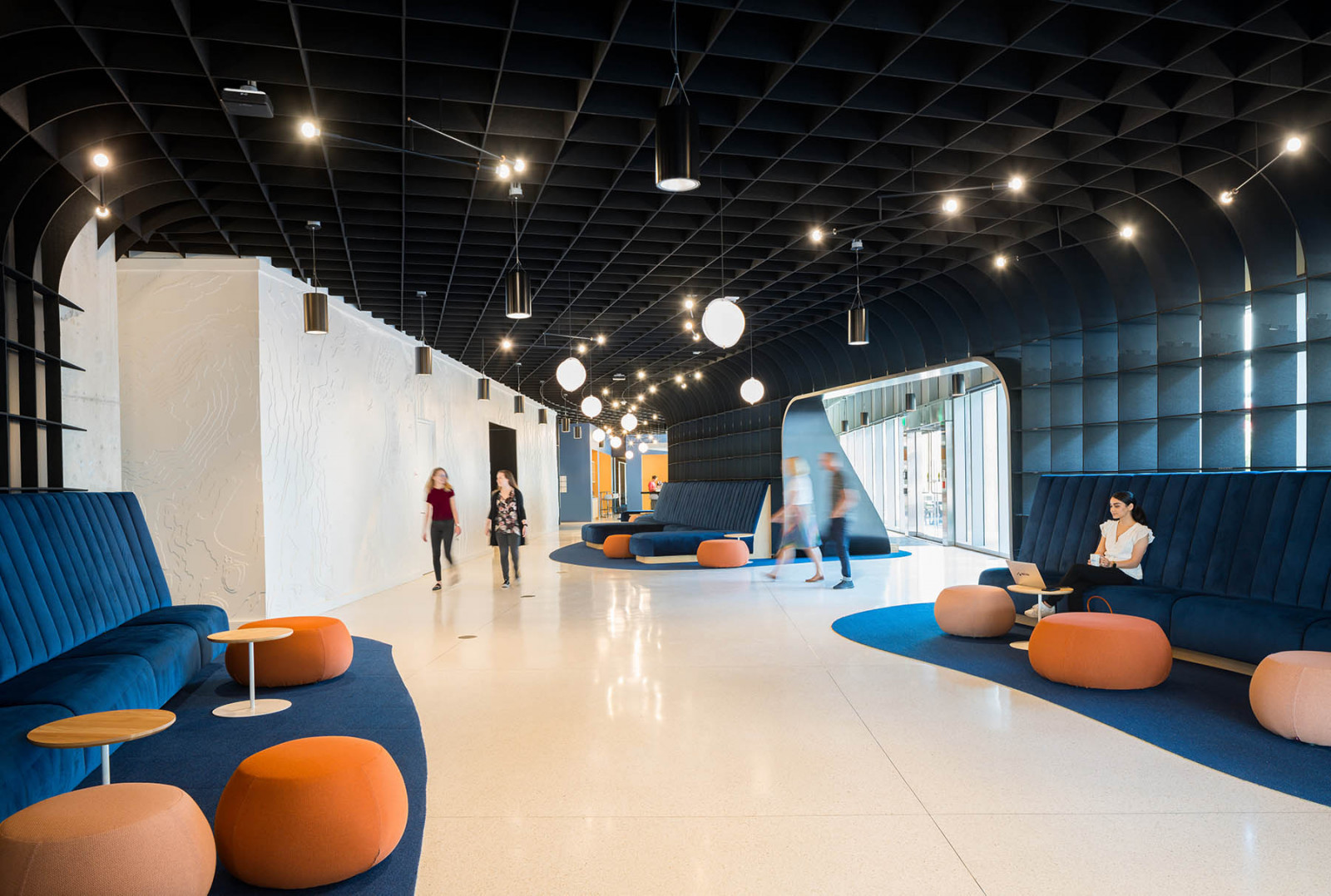 This office lobby features blue sofas, wooden tables and orange, circular ottomans to serve as another seating option. 