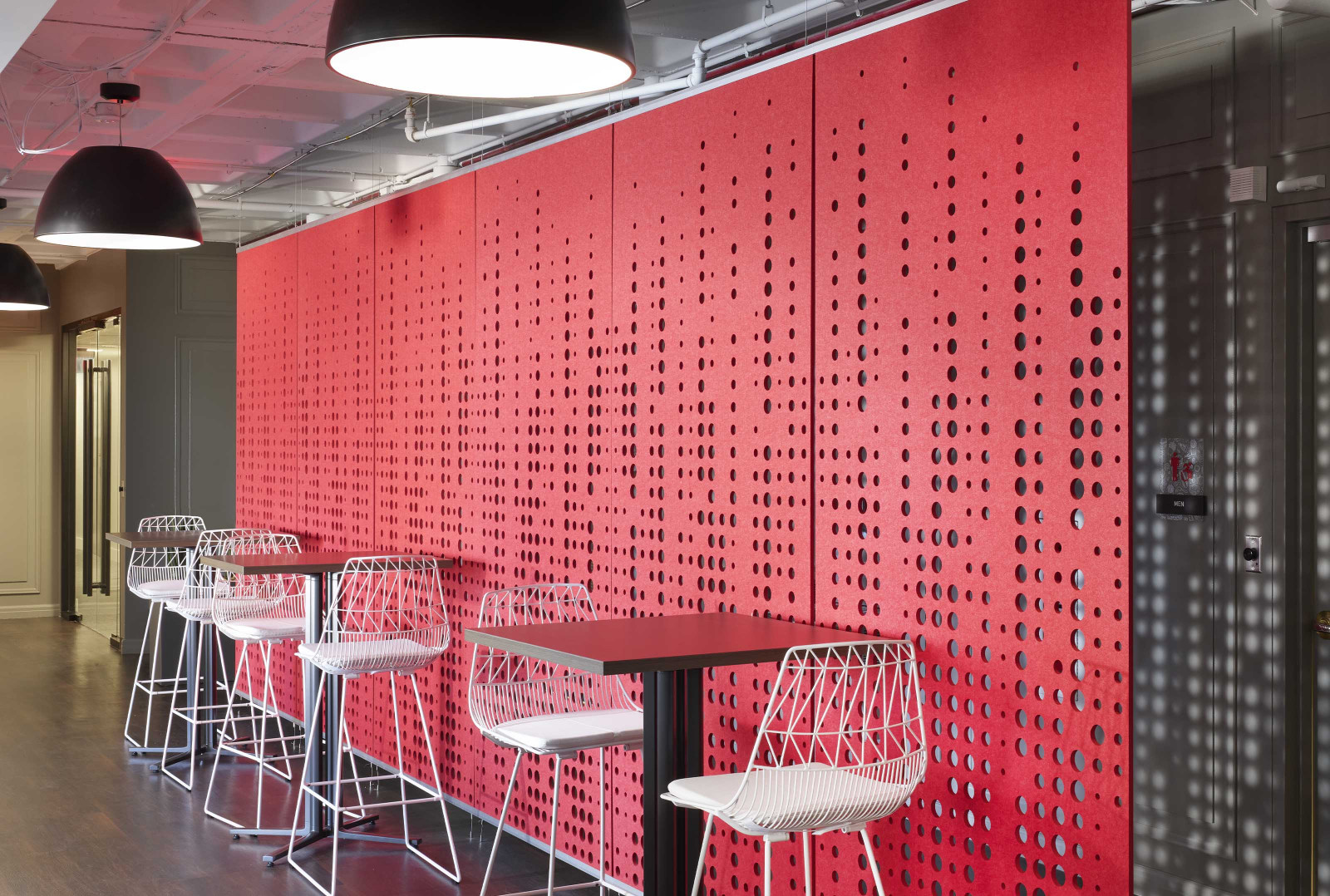 Red Wall panels with three different black tables with white chairs in front of the paneling.